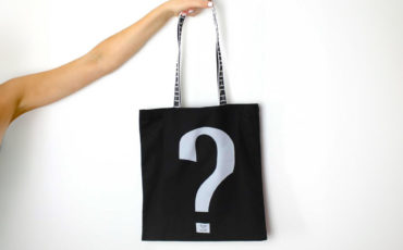 Person holding a black bag with a white question mark on a white background