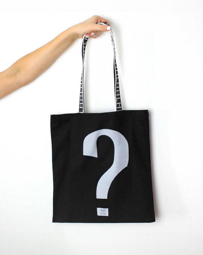 Person holding a black bag with a white question mark on a white background