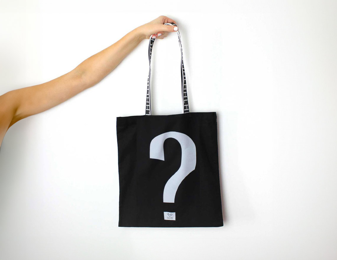 Person holding a black bag with a white question mark on a white background